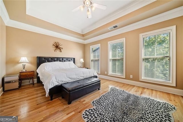 bedroom featuring light hardwood / wood-style floors, ornamental molding, a tray ceiling, and ceiling fan