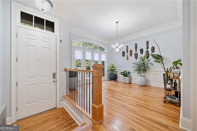 foyer entrance with an inviting chandelier, ornamental molding, and wood-type flooring