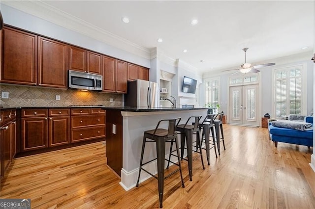 kitchen featuring a kitchen breakfast bar, light hardwood / wood-style floors, stainless steel appliances, ornamental molding, and a center island with sink