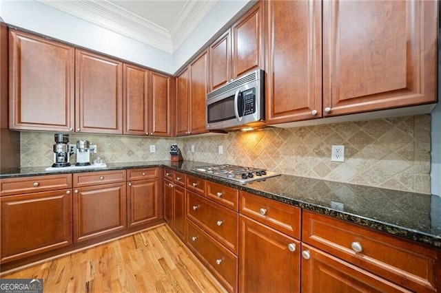 kitchen with appliances with stainless steel finishes, light hardwood / wood-style flooring, decorative backsplash, and dark stone counters