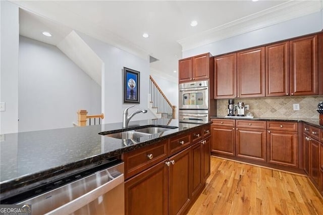 kitchen with sink, light hardwood / wood-style floors, stainless steel appliances, dark stone counters, and decorative backsplash