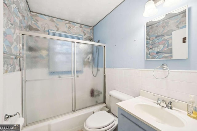 full bathroom with toilet, bath / shower combo with glass door, vanity, and tile walls