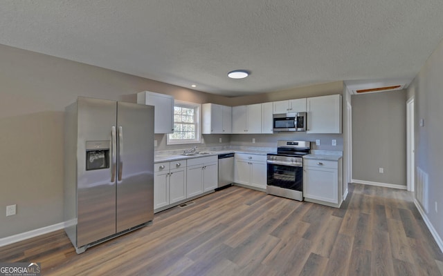 kitchen with white cabinets, dark hardwood / wood-style flooring, a textured ceiling, sink, and stainless steel appliances