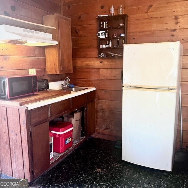 kitchen featuring white fridge, sink, and wood walls