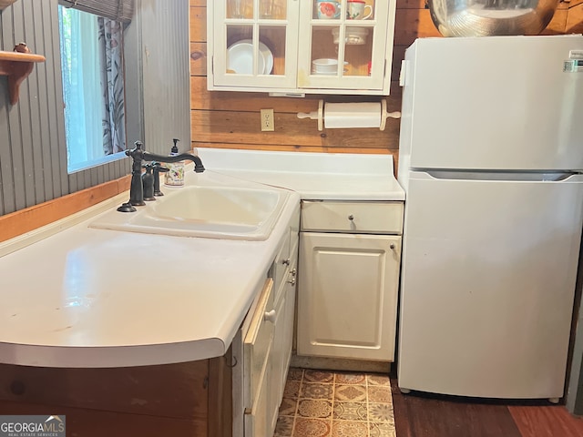 kitchen featuring white refrigerator, white cabinetry, wooden walls, and sink