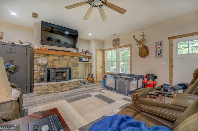 living room featuring a wood stove, ceiling fan, light wood-type flooring, and plenty of natural light