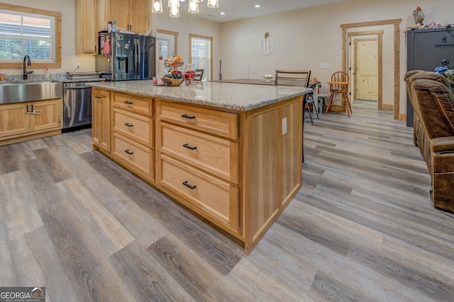 kitchen with a kitchen island, light hardwood / wood-style flooring, stainless steel appliances, sink, and light stone counters