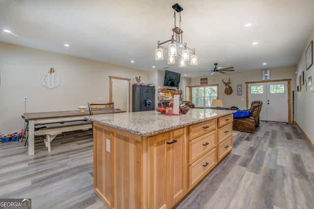 kitchen with light brown cabinetry, light wood-type flooring, a center island, ceiling fan, and decorative light fixtures