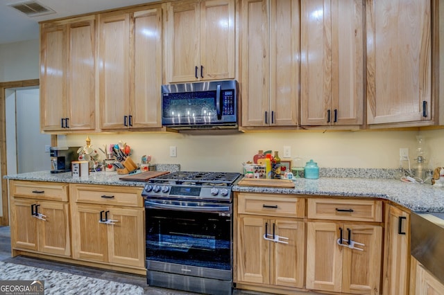 kitchen featuring black gas stove, light stone countertops, and light brown cabinetry