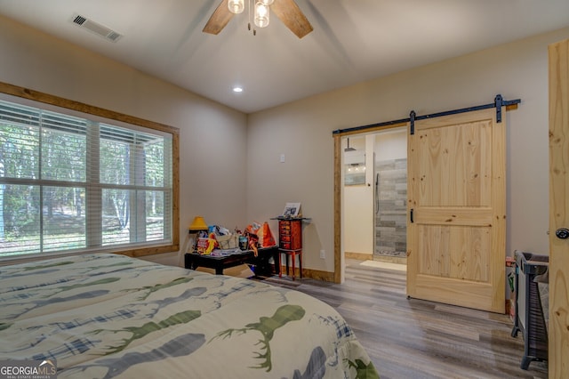 bedroom with ensuite bathroom, a barn door, hardwood / wood-style flooring, and ceiling fan