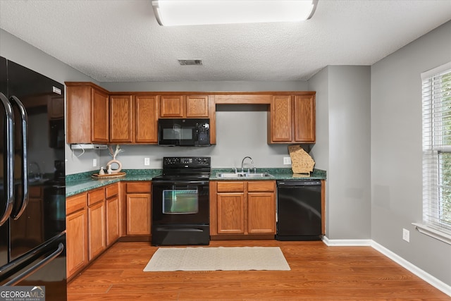 kitchen with light hardwood / wood-style floors, a textured ceiling, black appliances, and sink