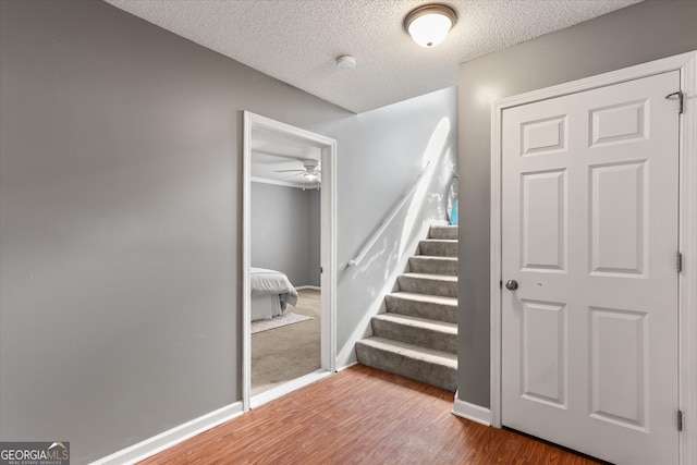 staircase with hardwood / wood-style floors, a textured ceiling, and ceiling fan