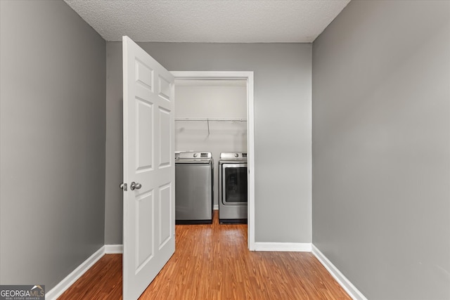 washroom featuring a textured ceiling, washing machine and clothes dryer, and light wood-type flooring