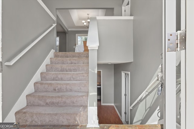 stairway with crown molding, wood-type flooring, and an inviting chandelier