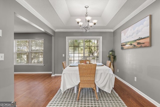 dining room featuring a notable chandelier, crown molding, hardwood / wood-style flooring, and a raised ceiling