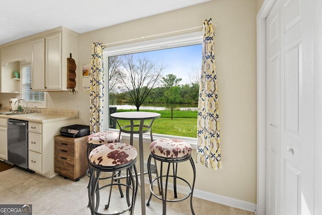 kitchen featuring sink, light tile patterned floors, dishwasher, a water view, and cream cabinetry