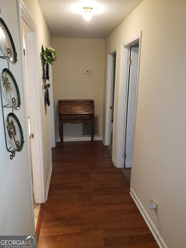 corridor featuring a textured ceiling and dark hardwood / wood-style flooring