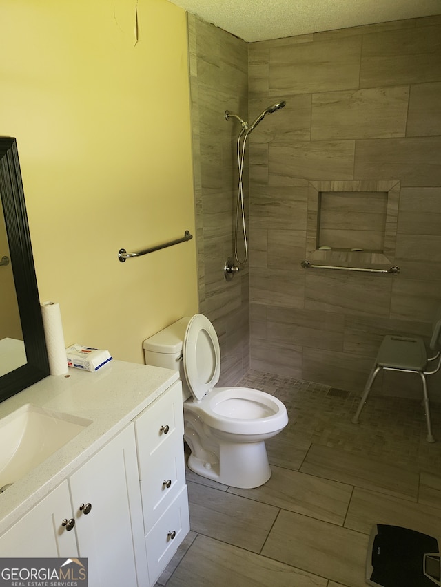 bathroom featuring vanity, a textured ceiling, toilet, and a tile shower