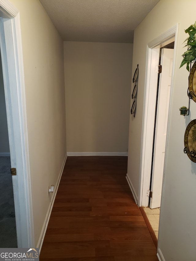 hallway with a textured ceiling and dark hardwood / wood-style flooring