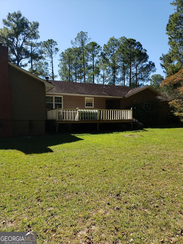 rear view of house featuring a wooden deck and a lawn