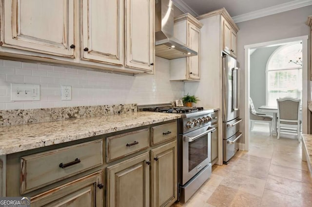 kitchen featuring premium appliances, decorative backsplash, wall chimney exhaust hood, light stone counters, and ornamental molding