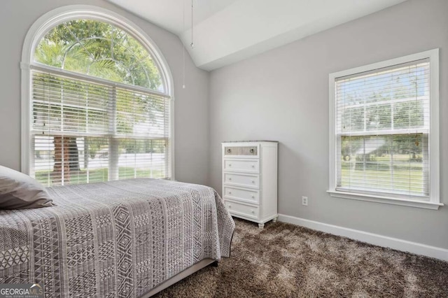 bedroom with dark carpet, lofted ceiling, and multiple windows