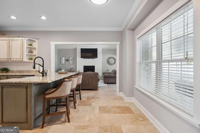 kitchen with a large fireplace, a kitchen bar, ornamental molding, sink, and light stone counters