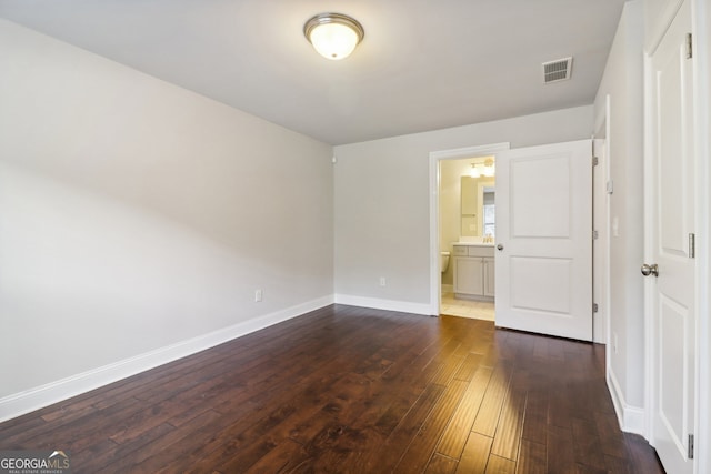 unfurnished bedroom featuring dark wood-type flooring and ensuite bathroom