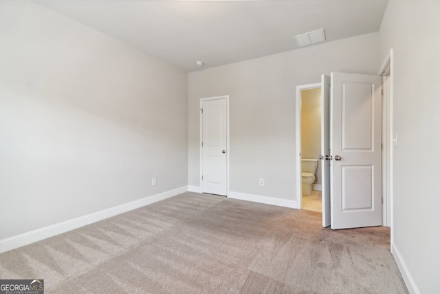 unfurnished bedroom featuring light carpet and ensuite bathroom