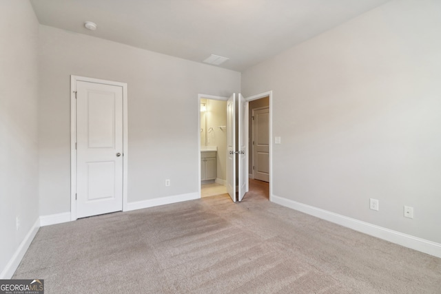 unfurnished bedroom featuring light carpet and ensuite bath