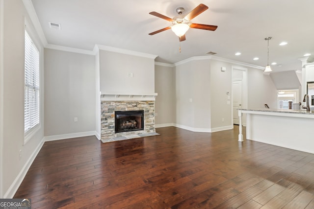 unfurnished living room with ceiling fan, a stone fireplace, dark hardwood / wood-style flooring, and crown molding