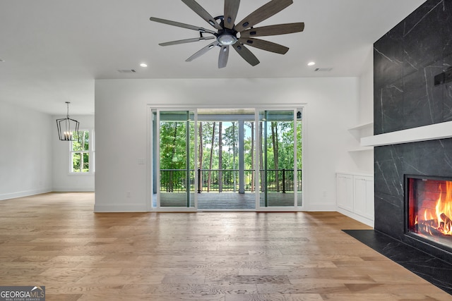 unfurnished living room featuring ceiling fan with notable chandelier, light hardwood / wood-style floors, plenty of natural light, and a fireplace