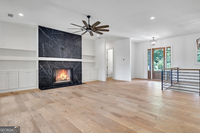 unfurnished living room with tile walls, a premium fireplace, built in features, and light wood-type flooring