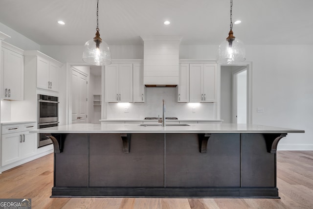 kitchen featuring a large island, white cabinetry, light hardwood / wood-style floors, decorative light fixtures, and stainless steel double oven