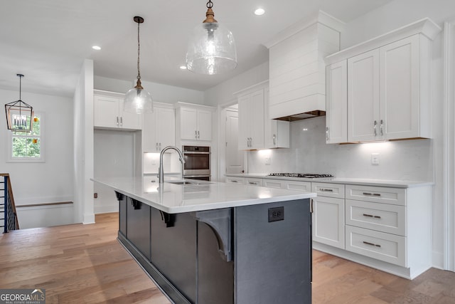 kitchen with sink, a kitchen island with sink, light hardwood / wood-style flooring, and pendant lighting