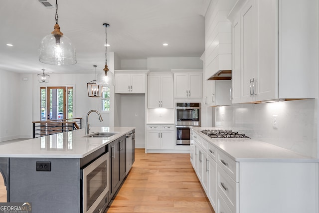 kitchen with appliances with stainless steel finishes, white cabinets, decorative light fixtures, and a center island with sink