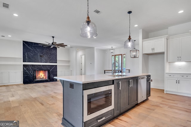 kitchen featuring appliances with stainless steel finishes, sink, a fireplace, white cabinetry, and pendant lighting