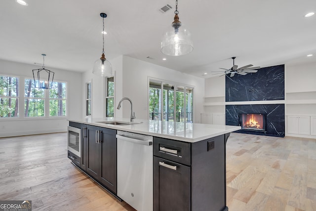 kitchen with pendant lighting, appliances with stainless steel finishes, a kitchen island with sink, and light wood-type flooring