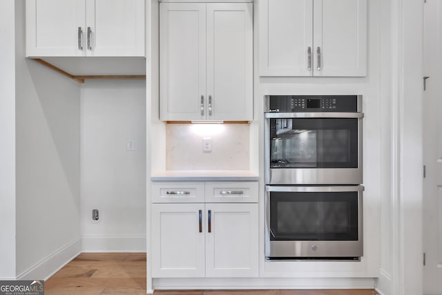 kitchen featuring stainless steel double oven, white cabinets, and light hardwood / wood-style flooring