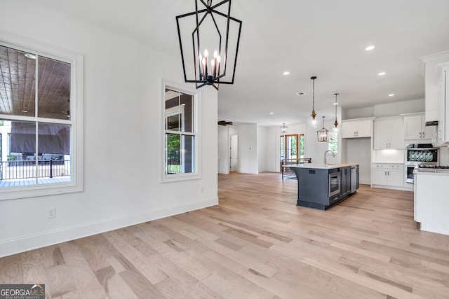 kitchen with an island with sink, light hardwood / wood-style flooring, pendant lighting, and white cabinets