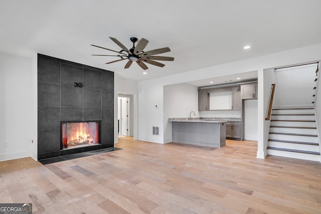 unfurnished living room featuring sink, a tile fireplace, light wood-type flooring, and ceiling fan