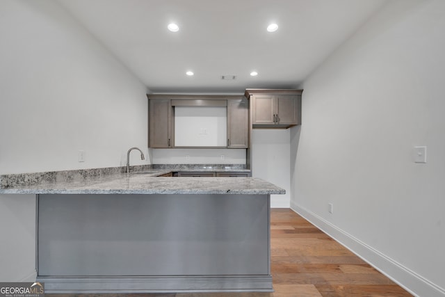 kitchen featuring light hardwood / wood-style flooring, kitchen peninsula, light stone counters, and sink