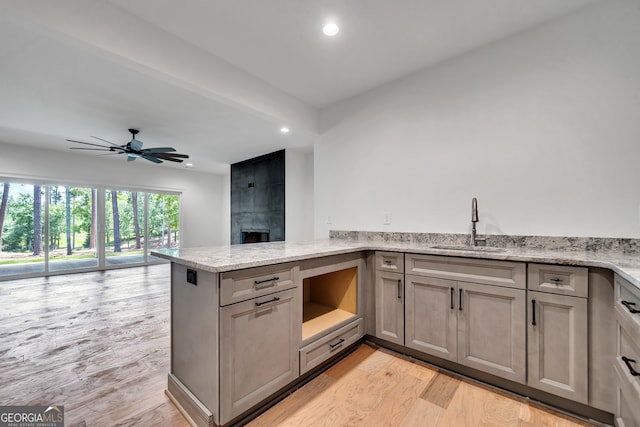 kitchen featuring kitchen peninsula, light stone counters, a fireplace, light hardwood / wood-style floors, and ceiling fan