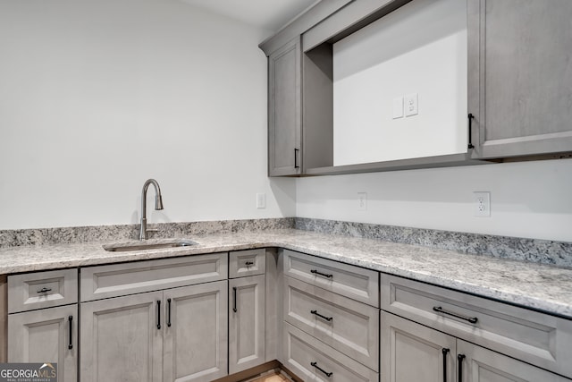 kitchen featuring sink, light stone counters, and gray cabinetry