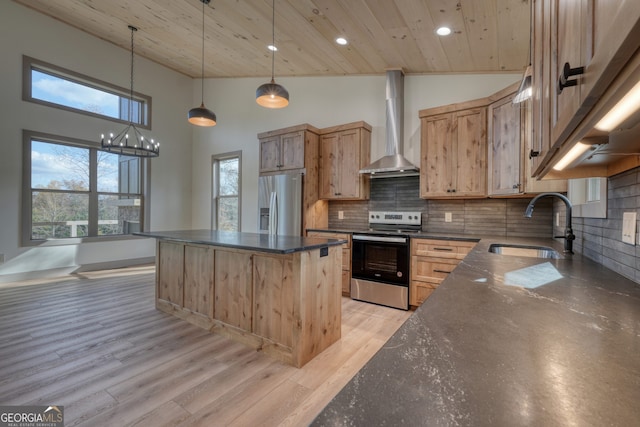 kitchen featuring appliances with stainless steel finishes, high vaulted ceiling, light hardwood / wood-style floors, wall chimney exhaust hood, and a center island