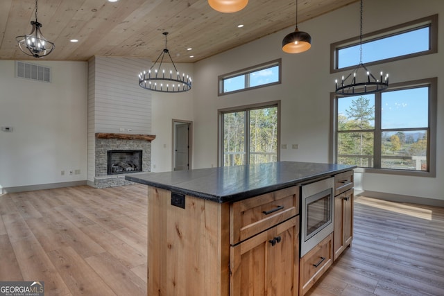 kitchen featuring light hardwood / wood-style flooring, stainless steel microwave, a center island, and high vaulted ceiling