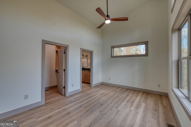 unfurnished bedroom featuring ensuite bathroom, high vaulted ceiling, and light wood-type flooring