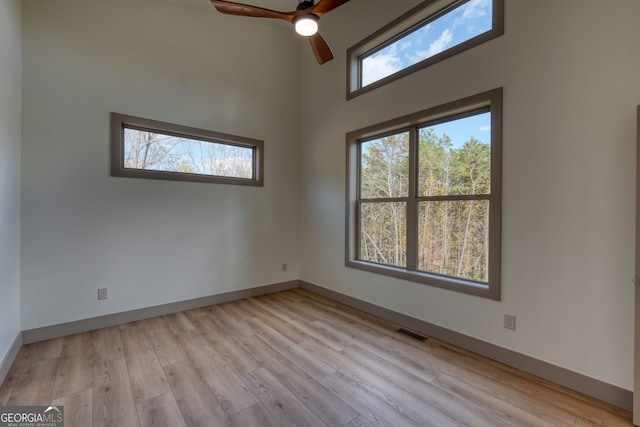 unfurnished room with light hardwood / wood-style floors, a high ceiling, and ceiling fan