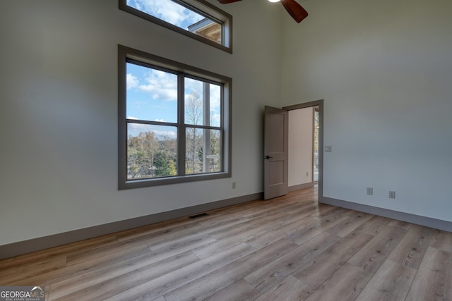 spare room featuring a towering ceiling, light wood-type flooring, and ceiling fan