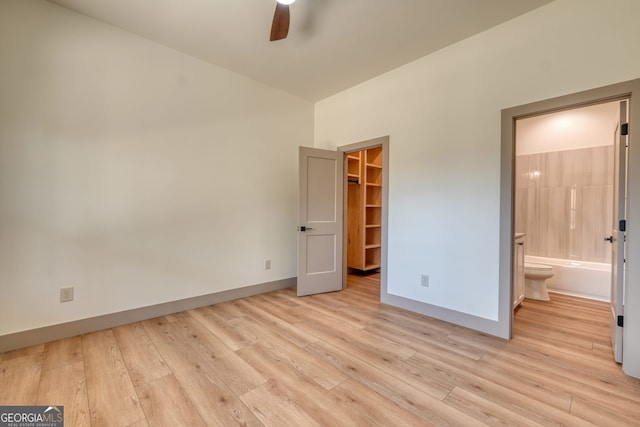 unfurnished bedroom with connected bathroom, ceiling fan, light hardwood / wood-style flooring, and a walk in closet